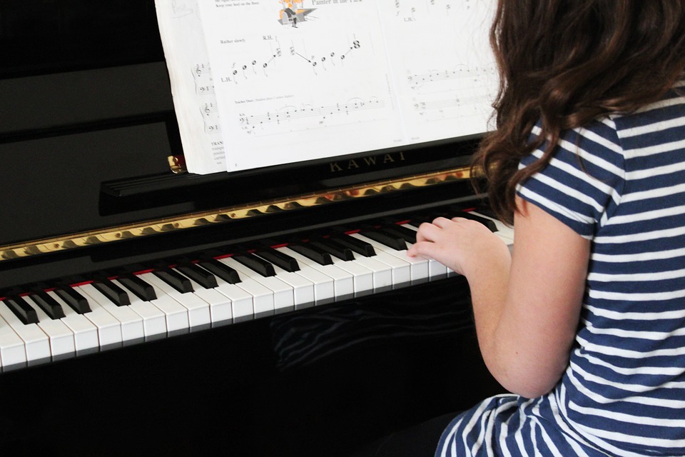 little girl playing the piano. Girl is wearing a striped dress